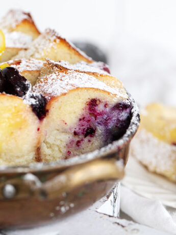 Blueberry lemon bread pudding in baking dish and spooned out onto a plate.