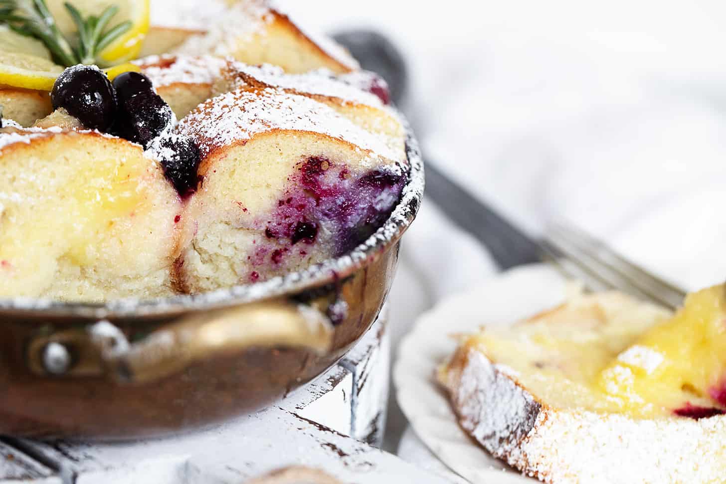Blueberry lemon bread pudding in baking dish and spooned out onto a plate.