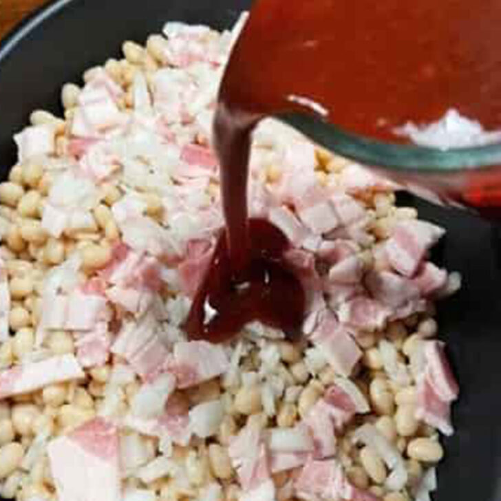 Pouring the sweet and sassy sauce over the beans and bacon in a casserole dish.