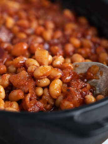sweet sassy baked beans in baking dish with spoon