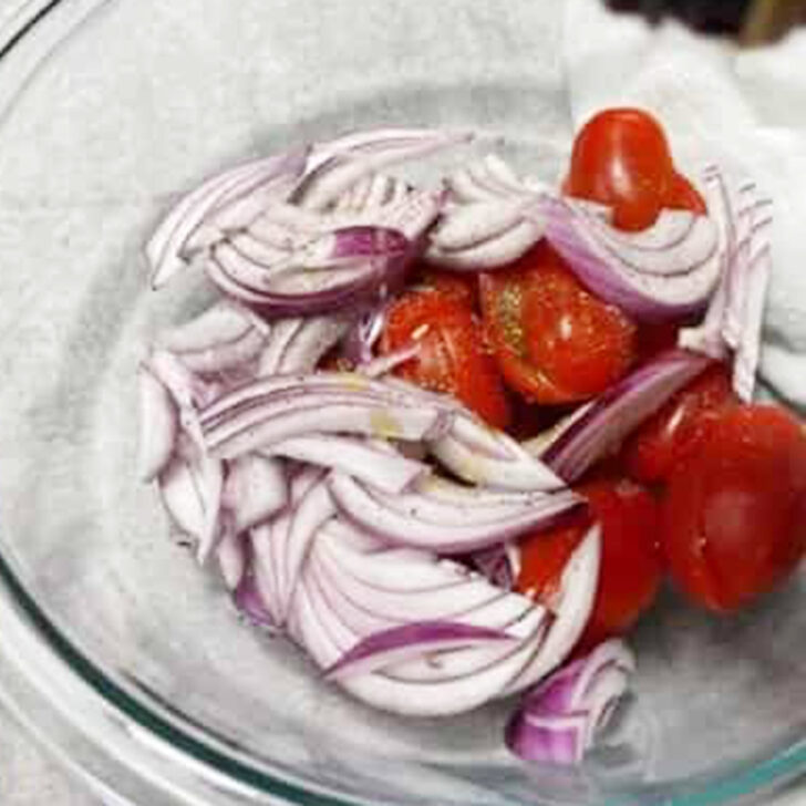 Cherry tomatoes and red onion mixture in a mixing bowl.