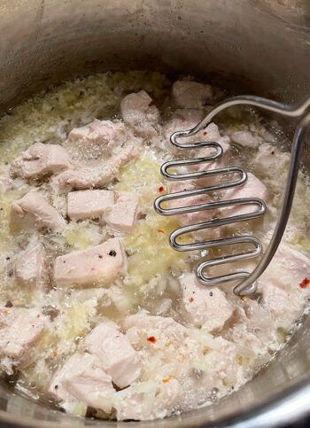 breaking up the chicken with a potato masher