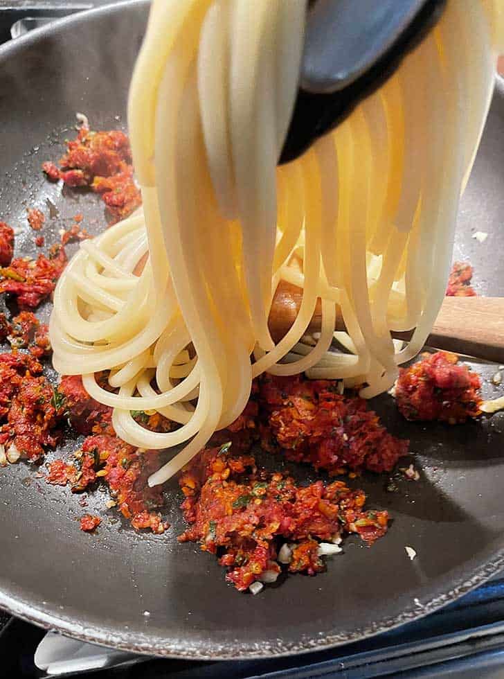 adding pasta to skillet with sun dried tomato and garlic