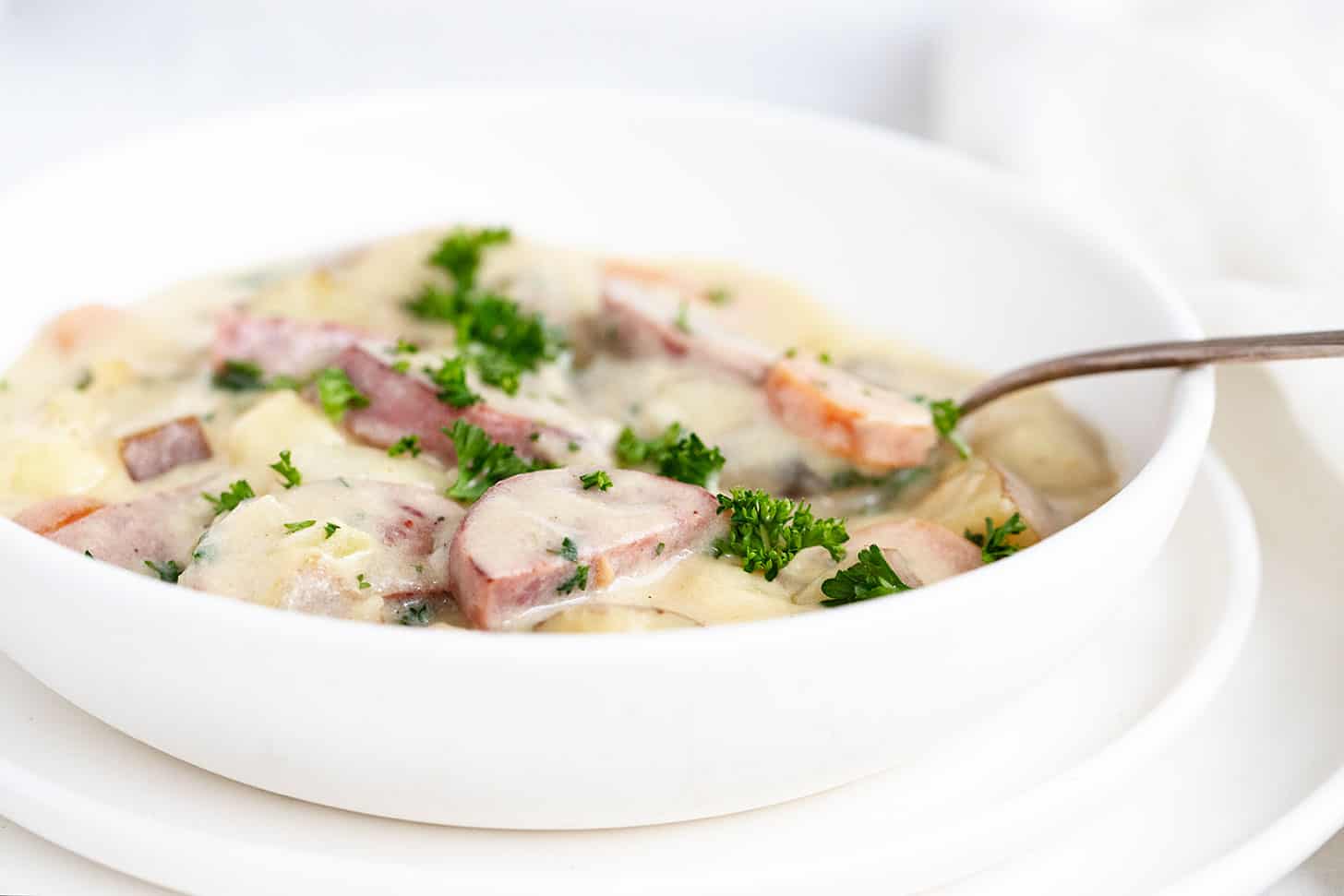 potato kielbassa soup in white bowl with spoon