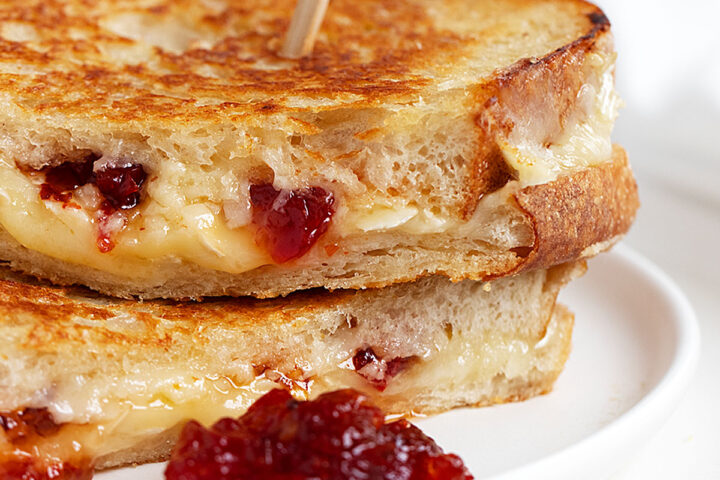 brie grilled cheese with red pepper jelly sliced on white plate