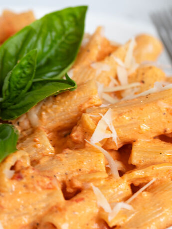creamy roasted red pepper pasta on plate with basil leaves