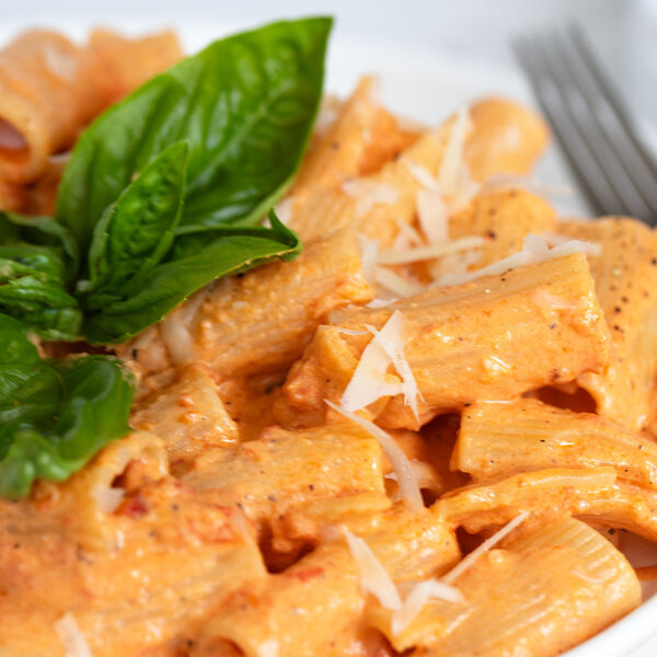 creamy roasted red pepper pasta on plate with basil leaves