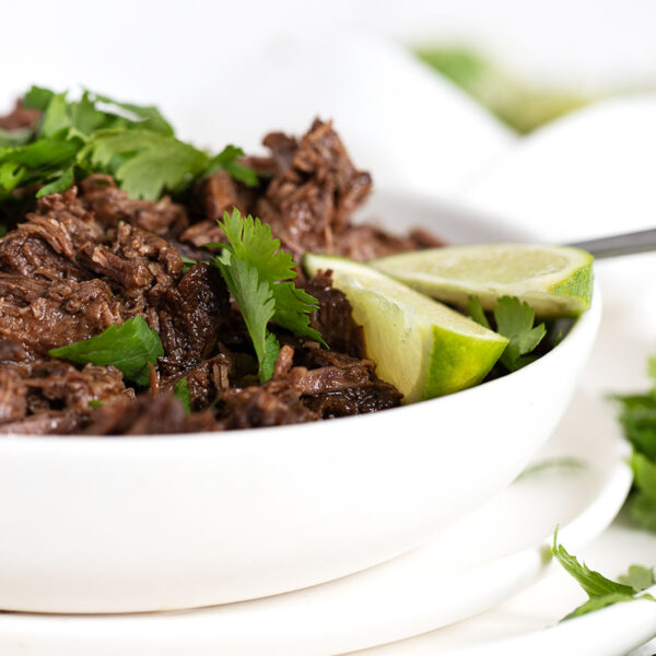 barbacoa in bowl with cilantro and limes