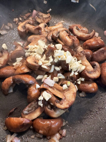 adding garlic to mushrooms in pan