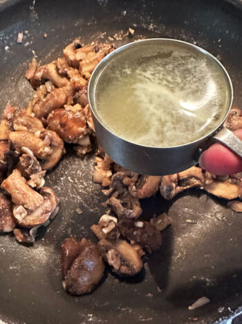 adding chicken broth to mushrooms in pan