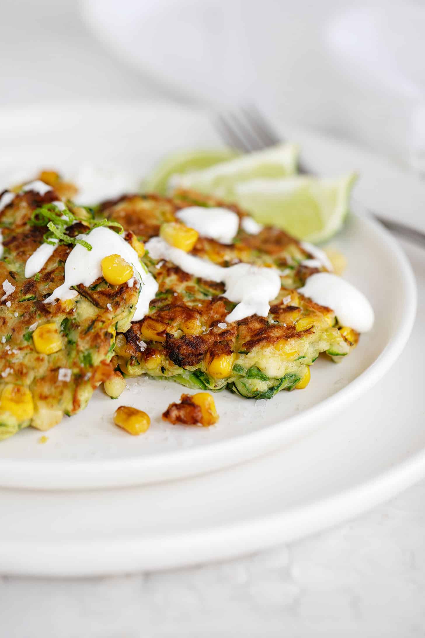 zucchini corn fritters on plate with sour cream drizzle