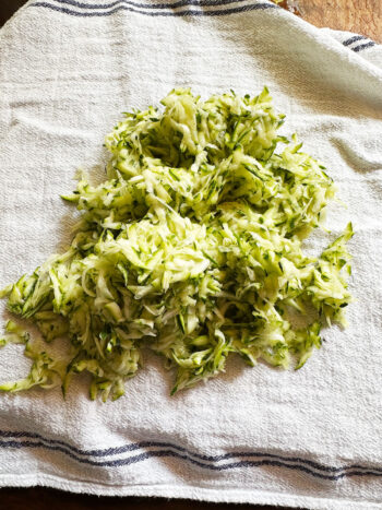 grated zucchini on tea towel before squeezing liquid out