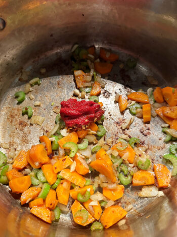 Adding tomato paste and red pepper flakes to pot with sauteed vegetables.
