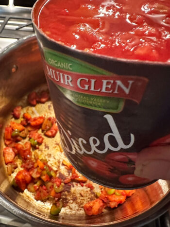 Adding canned diced tomatoes to the pot.