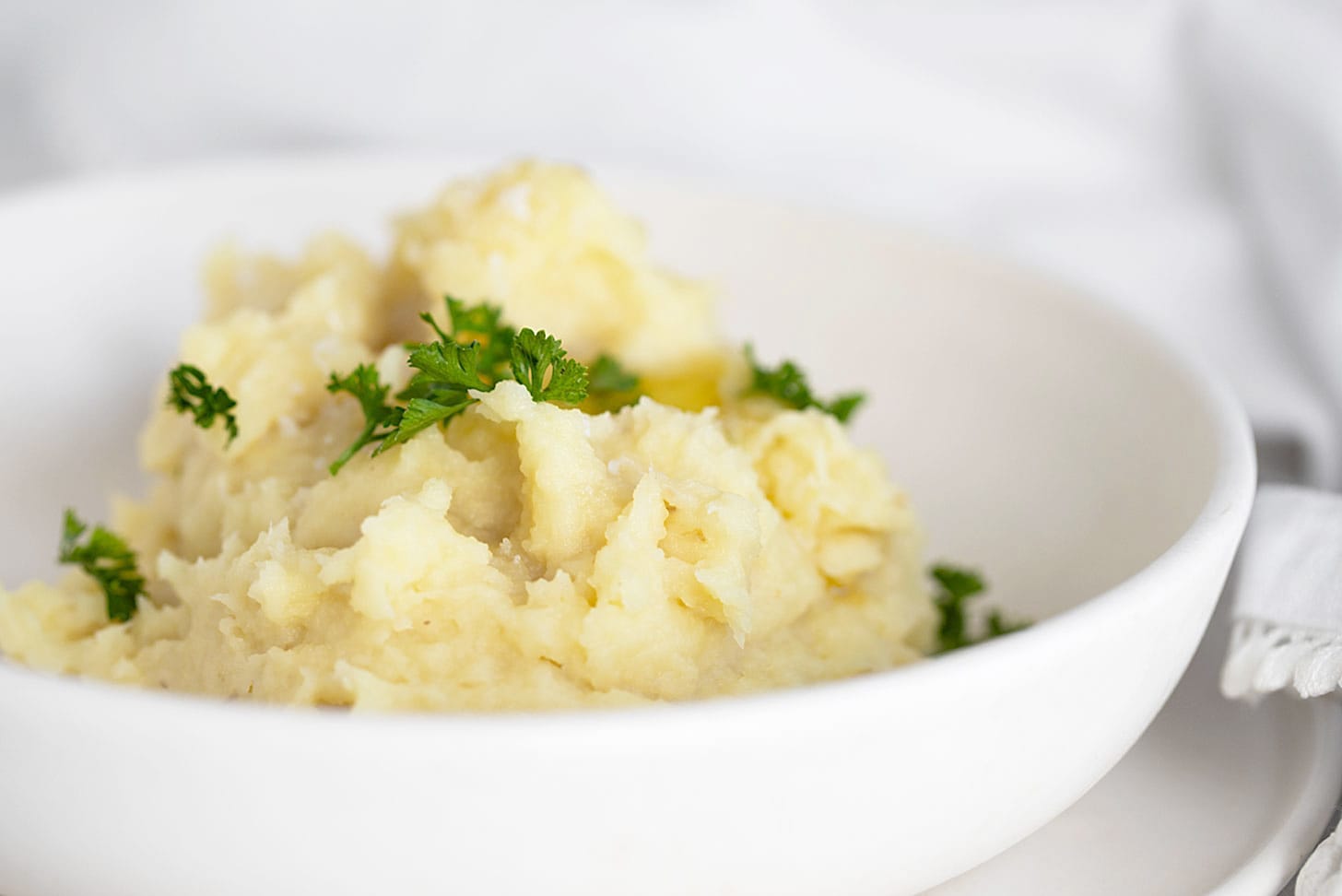 Parsnip puree in white bowl with parsley garnish.