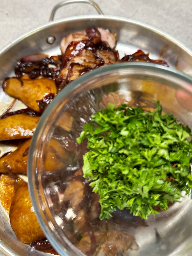 Pears and sliced pork on serving dish, with onions overtop and parsley ready to be garnished.