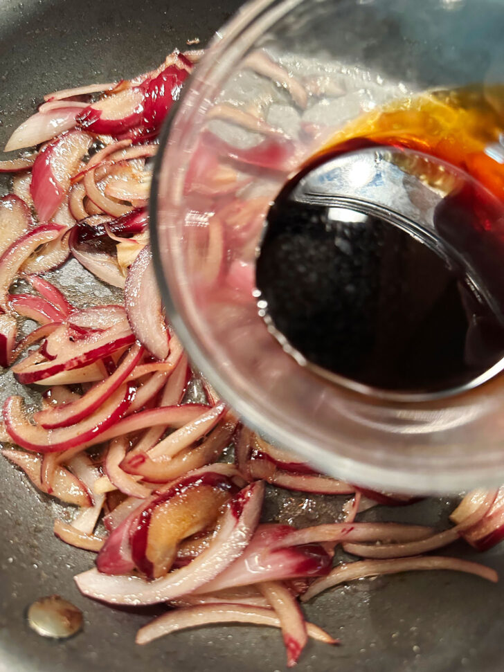 Adding balsamic vinegar to onions in skillet.