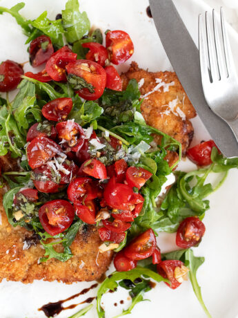 pork milanese on plate with arugula and tomatoes