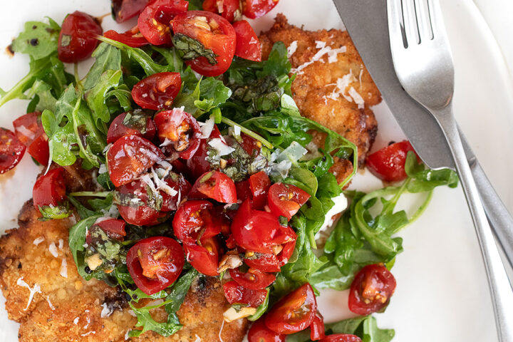 pork milanese on plate with arugula and tomatoes