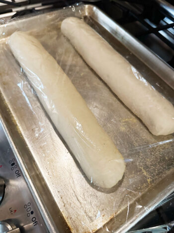 two rolled dough pieces on baking sheet covered with plastic wrap