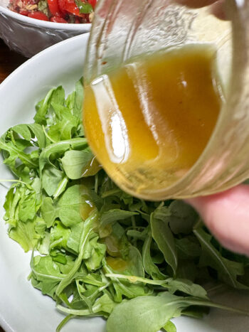 drizzling dressing over arugula