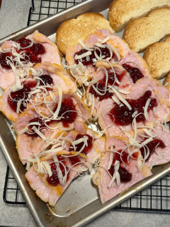 topping bread slices with peameal bacon, cranberry sauce and cheese