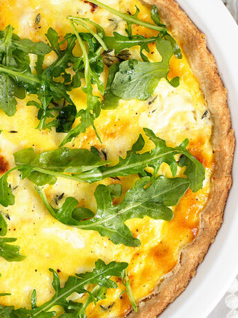goat cheese quiche in baking dish with arugula on top