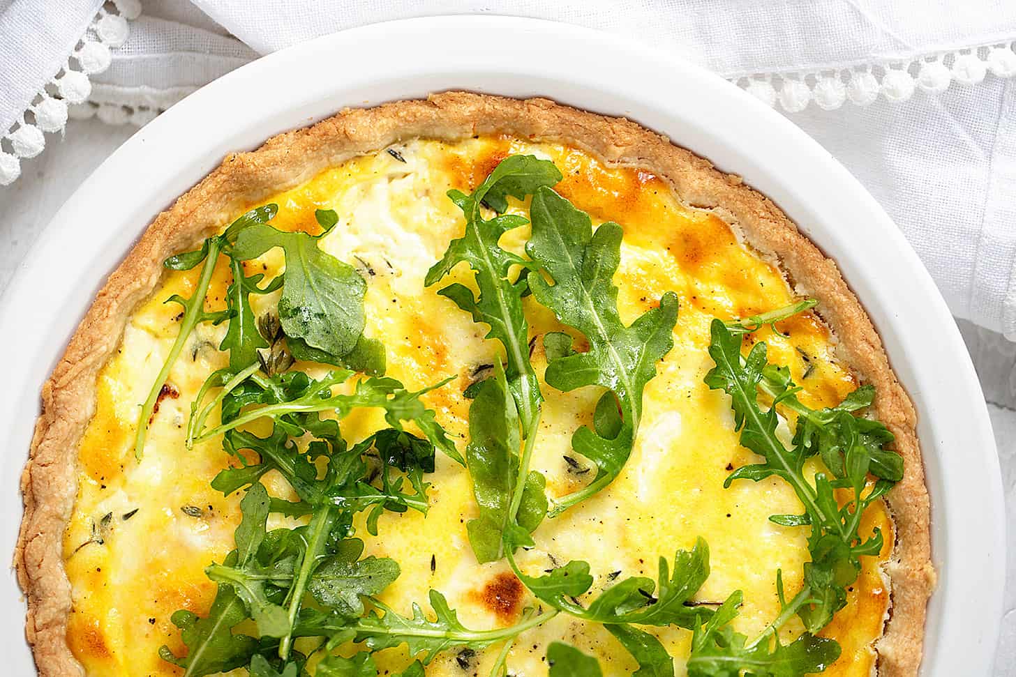 goat cheese quiche in baking dish with arugula on top