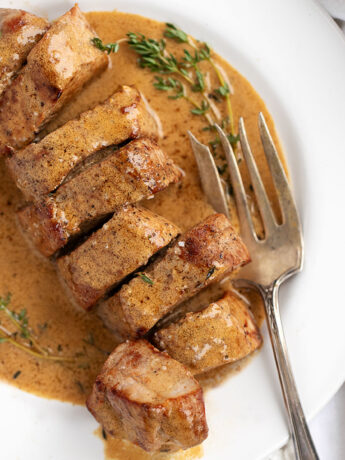pork tenderloin with mustard sauce on white plate with fork