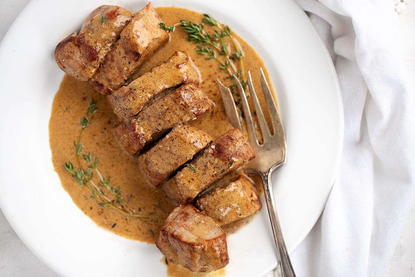 pork tenderloin with mustard sauce on white plate with fork
