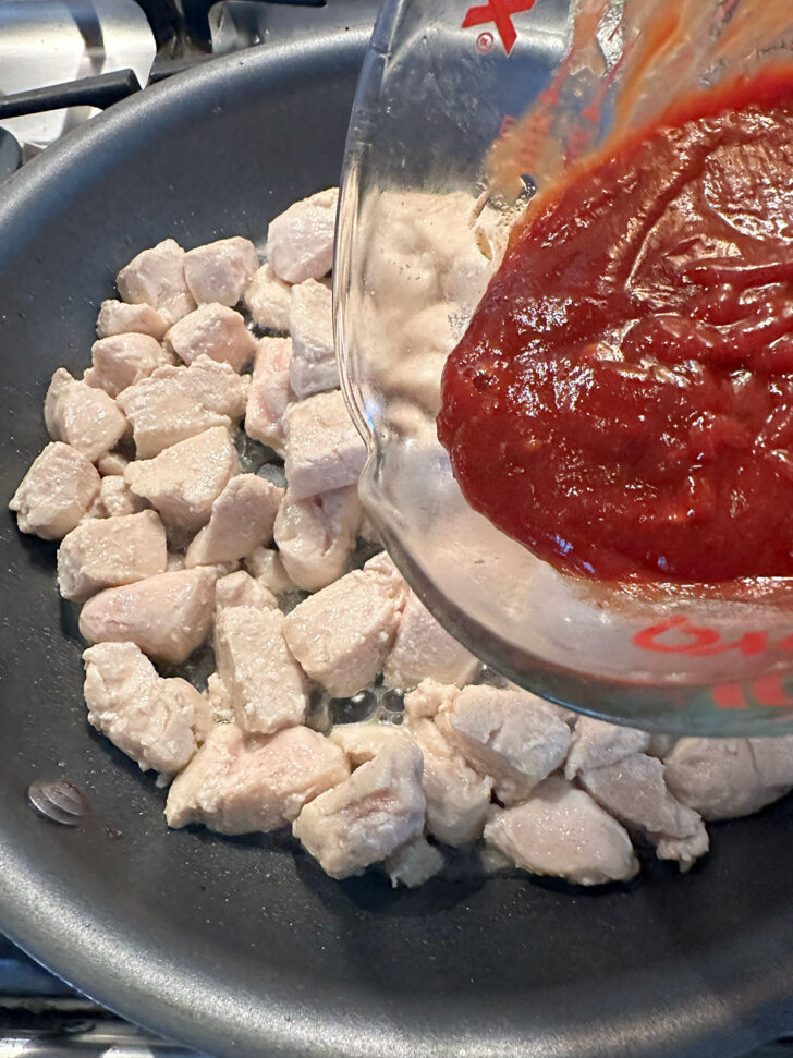 Adding the sauce to the cooked chicken.
