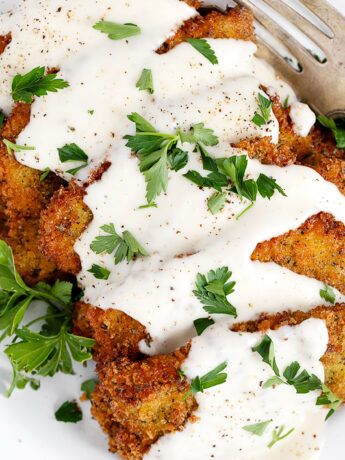 Pork scallopini topped with mornay sauce on white plate.
