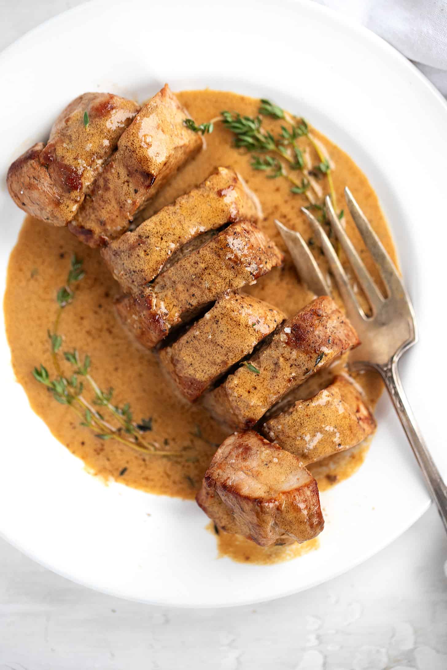 pork tenderloin with mustard sauce on white place with thyme sprigs