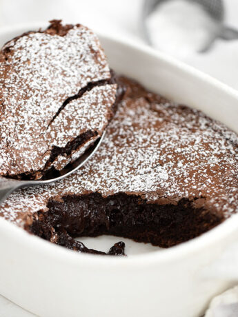 Warm brownie cake in baking dish with spoon.
