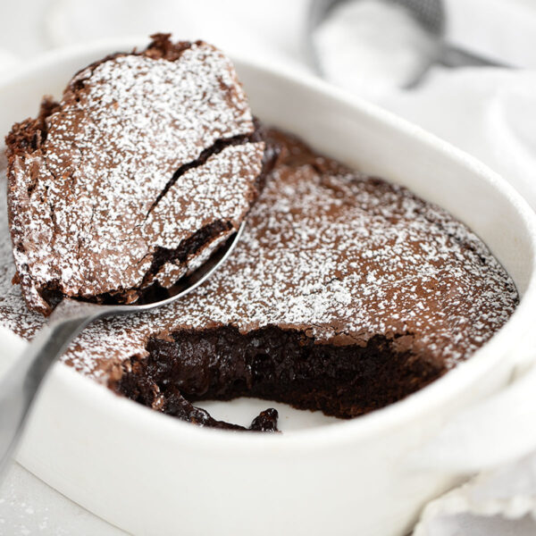 Warm brownie cake in baking dish with spoon.