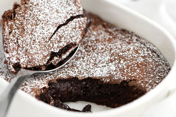 Warm brownie cake in baking dish with spoon.