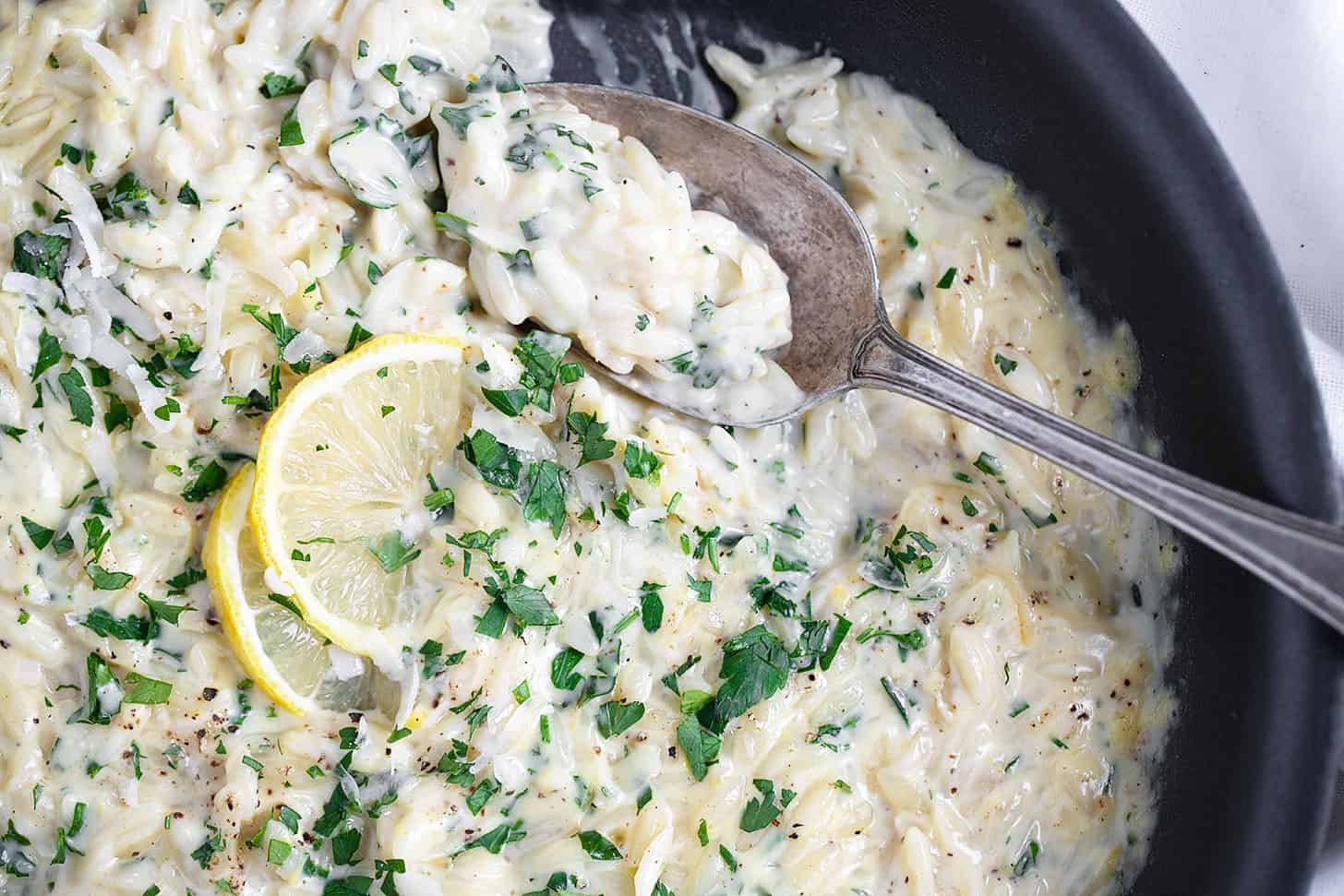 Creamy lemon parmesan orzo in skillet with spoon.