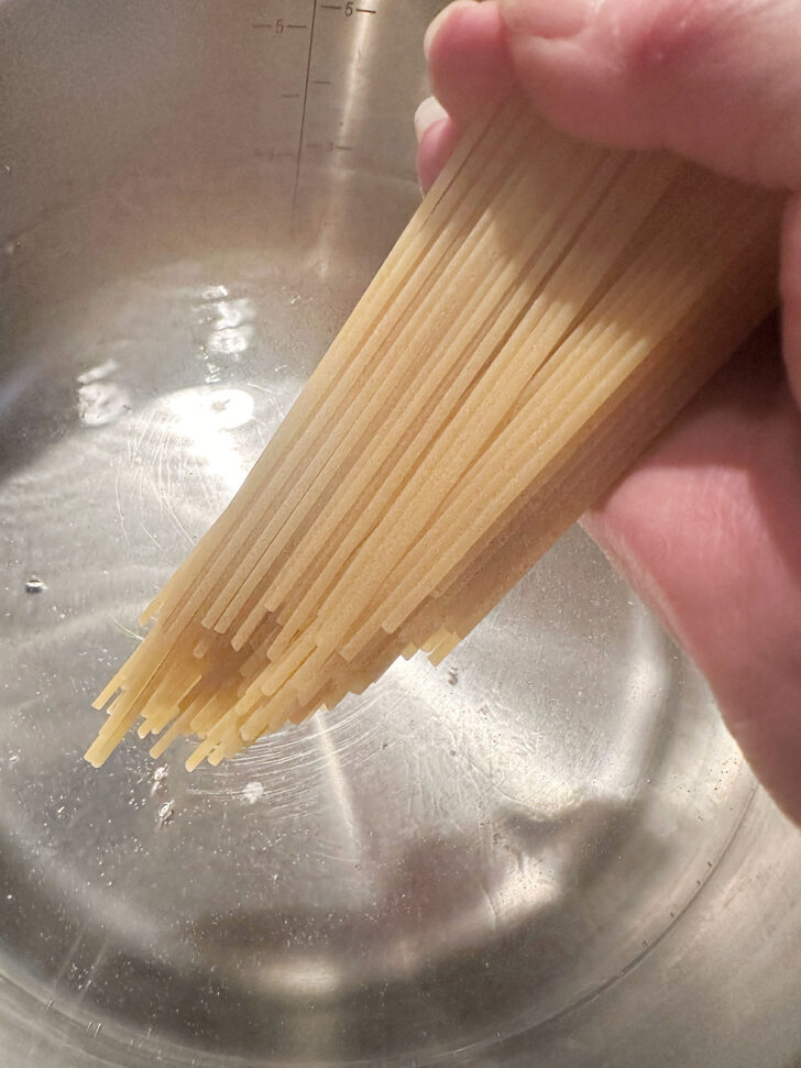 Adding dried pasta to boiling water.