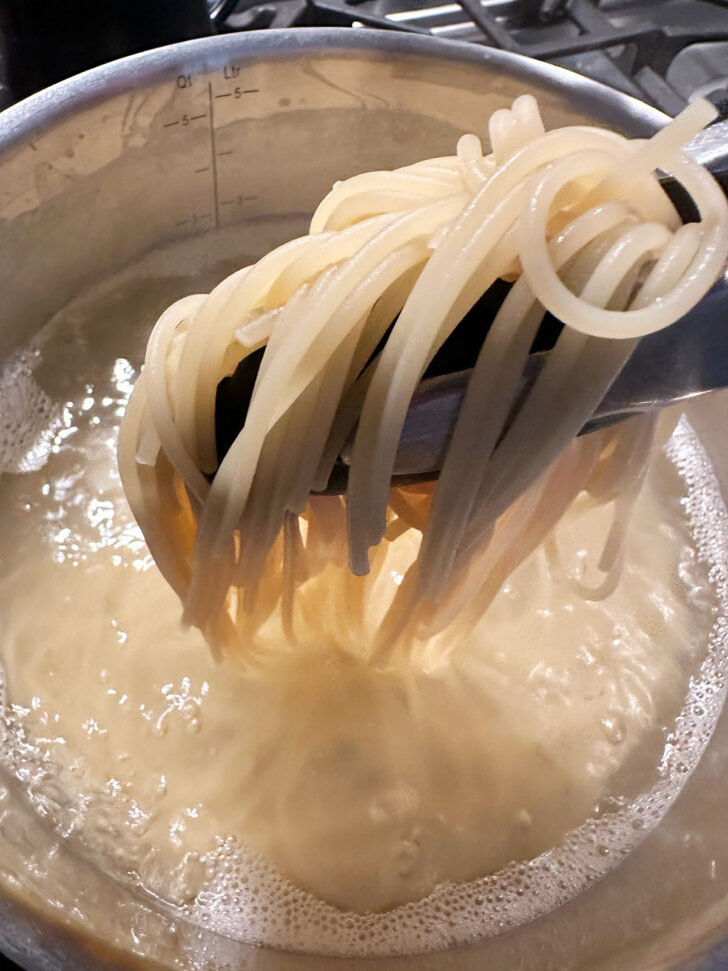 Removing pasta with tongs after cooking.