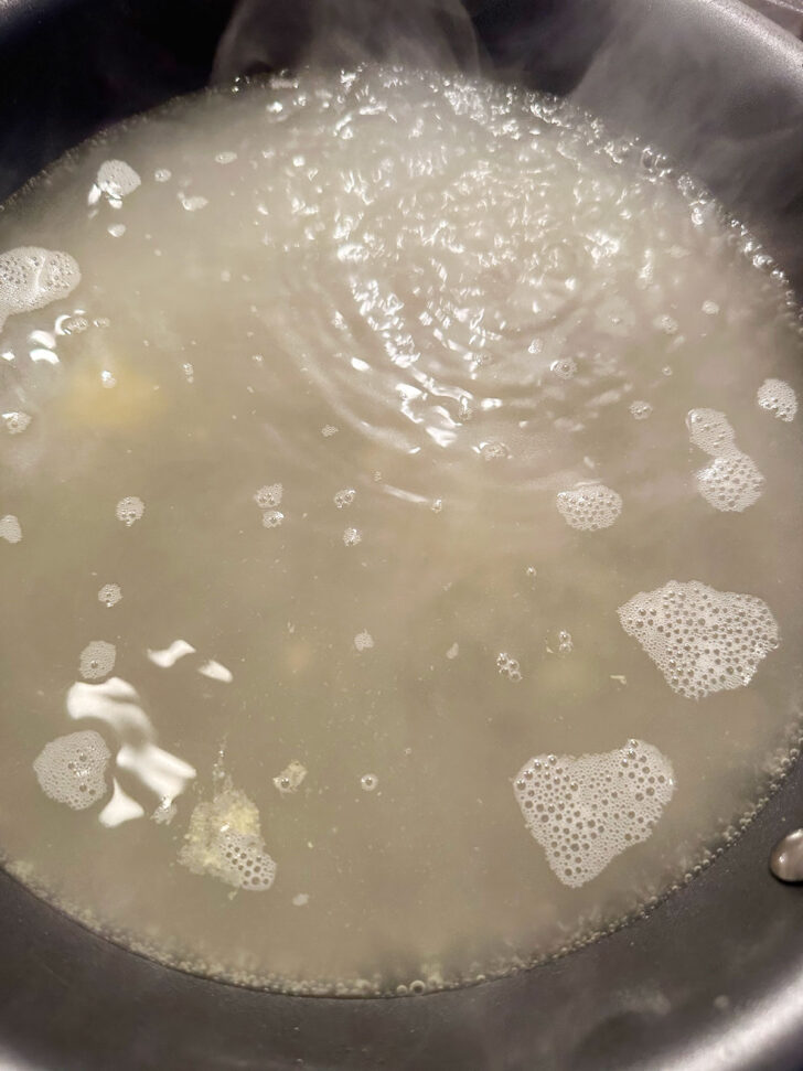 Chicken broth coming to a boil in skillet,