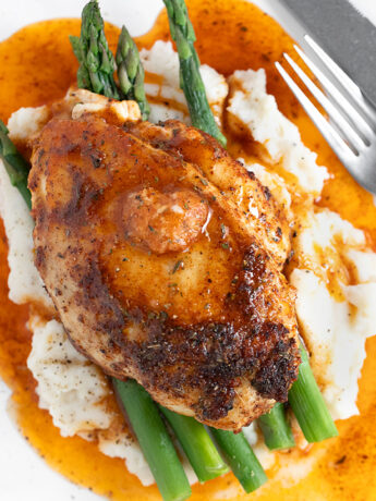 Cajun chicken on plate with asparagus and mashed potatoes.