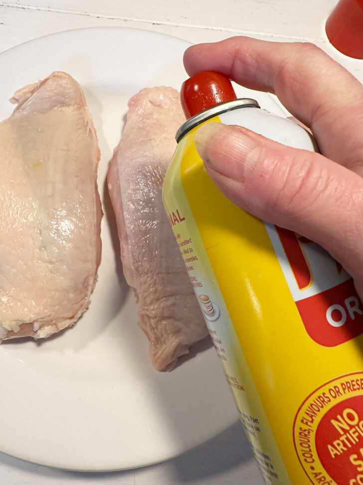 Spraying the chicken breast with cooking spray.