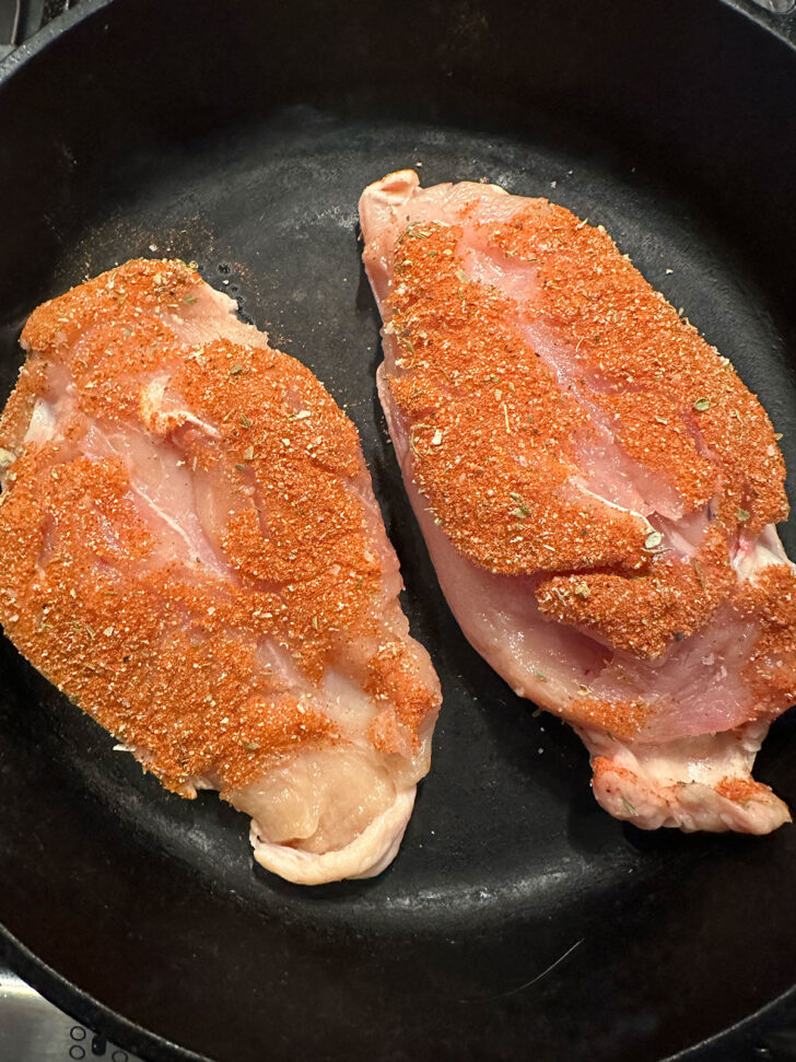 Coated chicken breasts in a cast iron skillet.