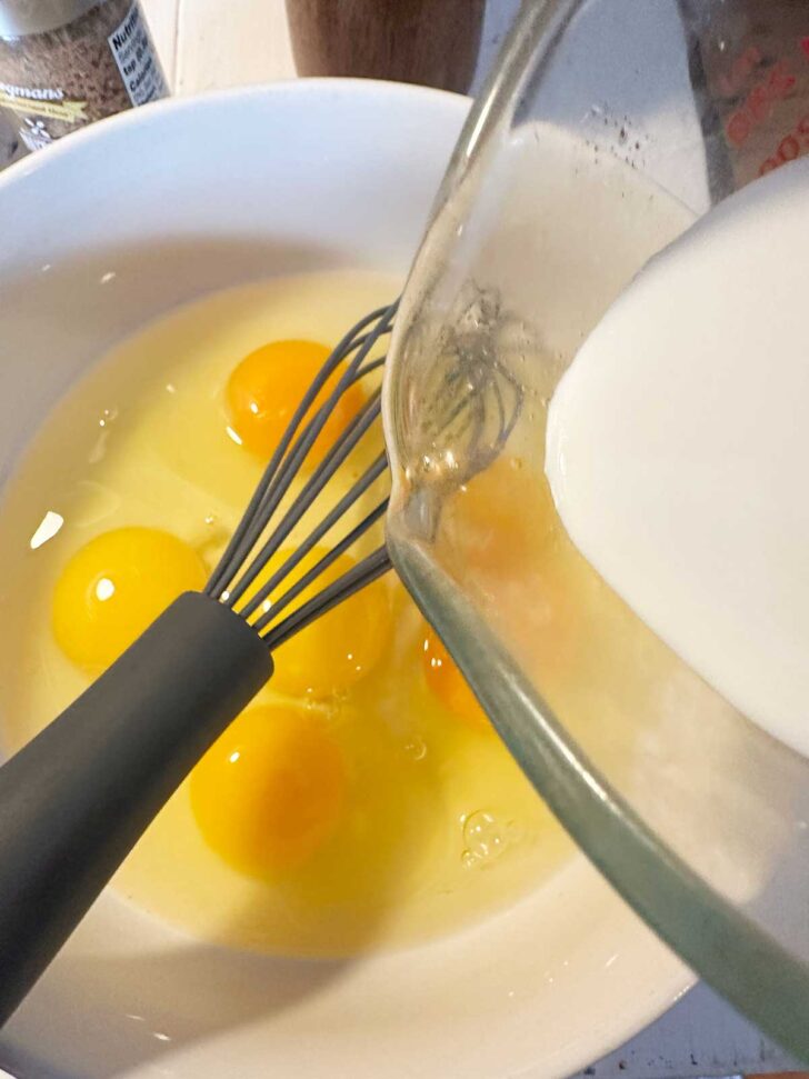 Adding milk to a bowl of eggs.