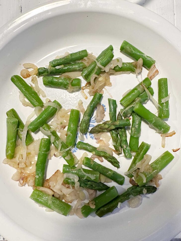Cooked shallots and asparagus in a pie plate.