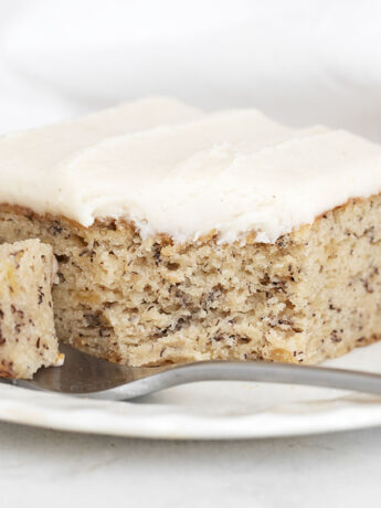 Slice of iced banana cake on plate with fork.