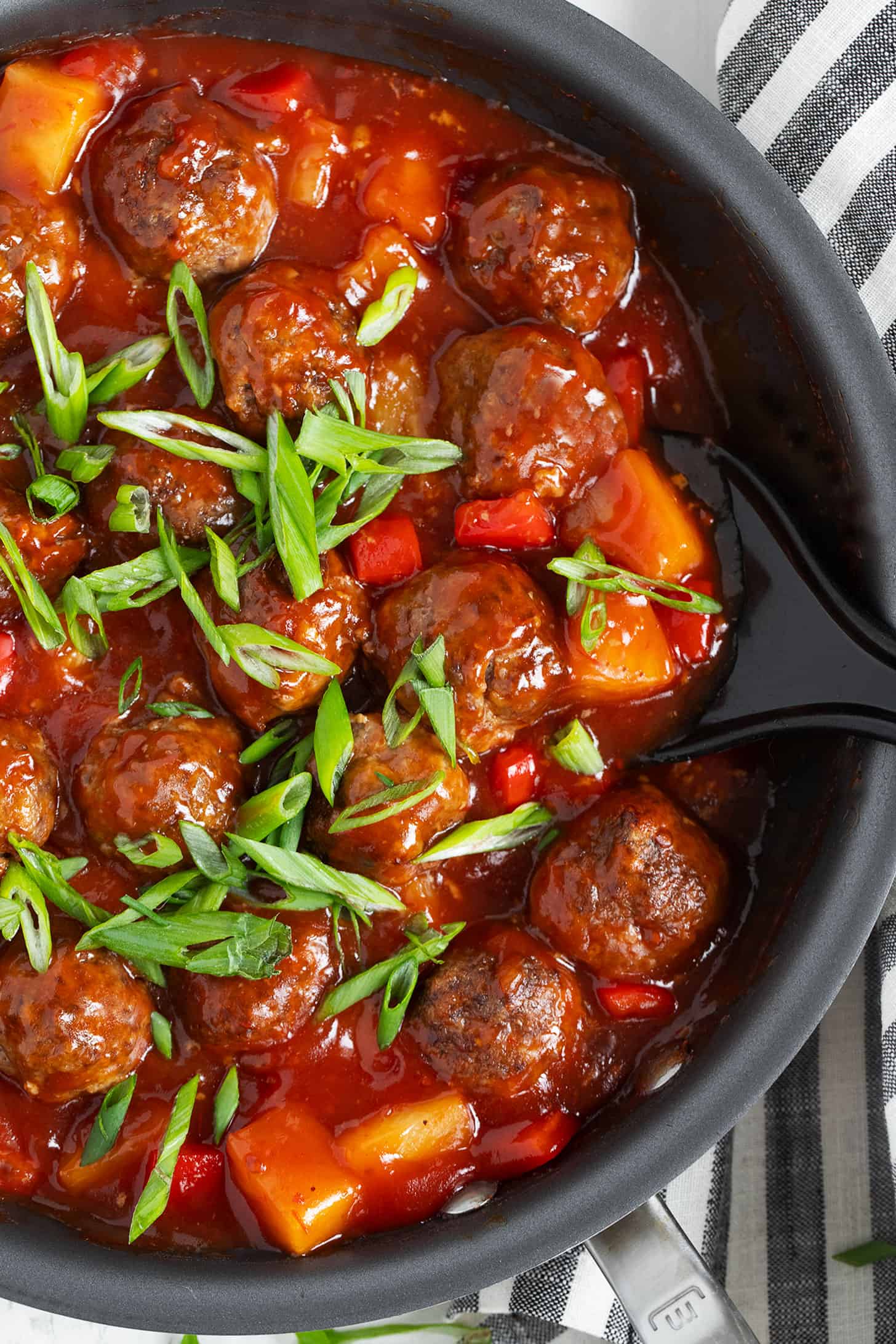 Pineapple meatballs in skillet with spoon.