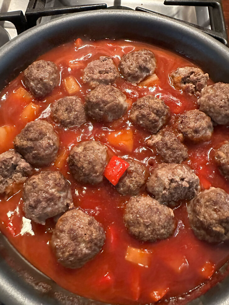 Adding cooked meatballs to the skillet with the sauce.