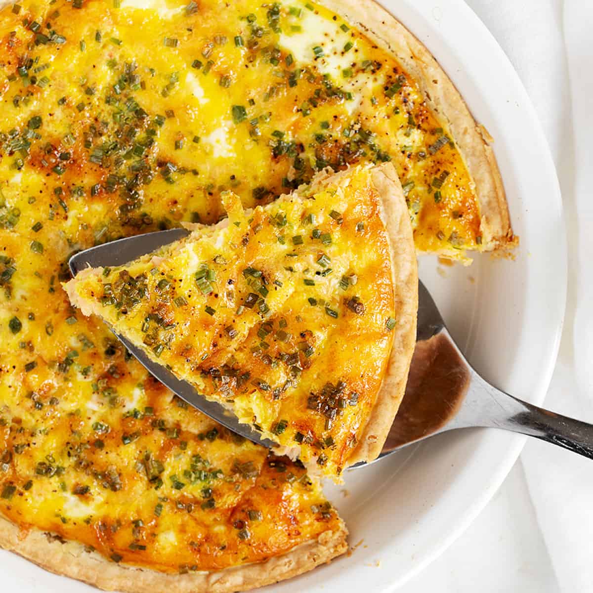 Salmon quiche in pie dish with a sliced on server.