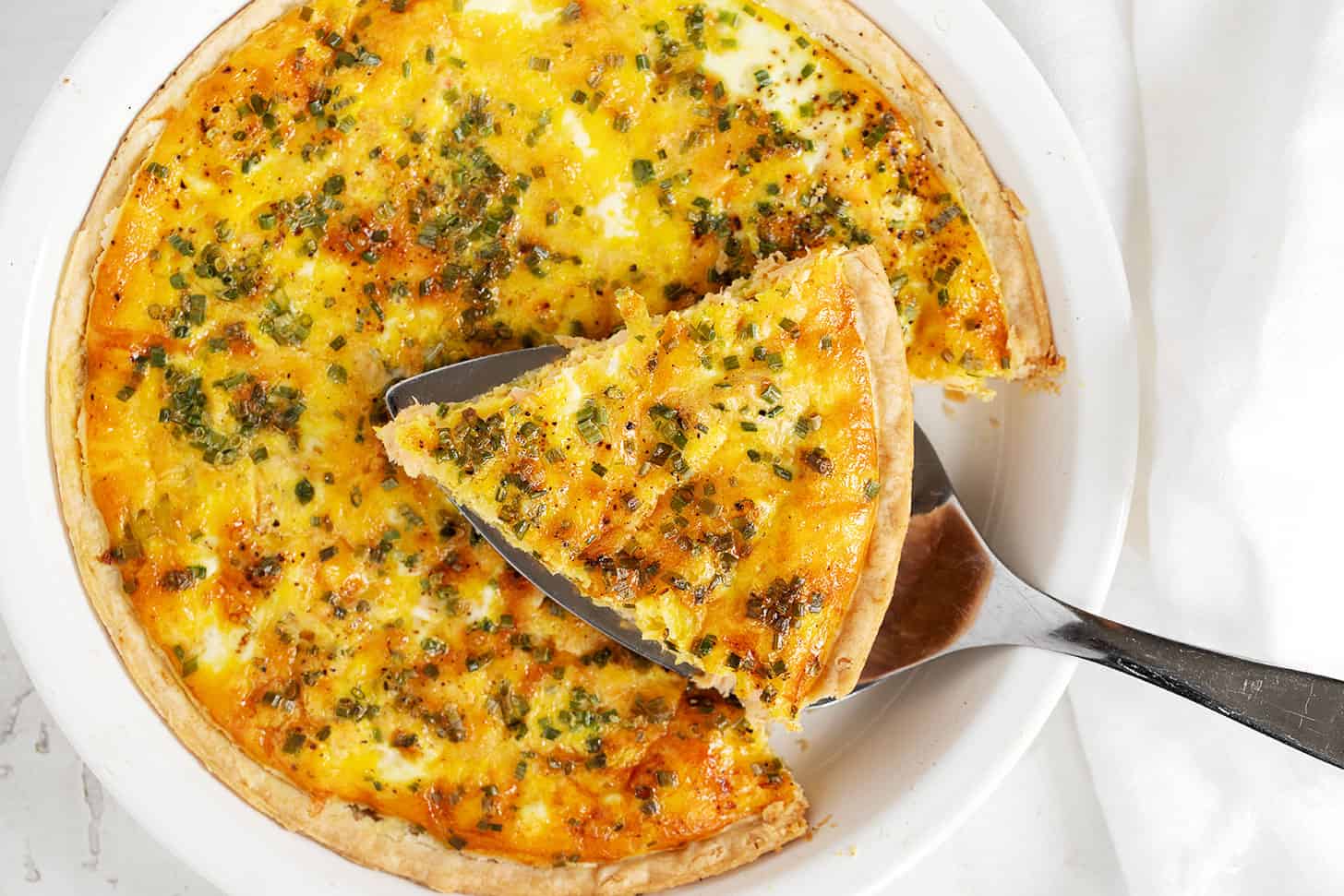 Salmon quiche in pie dish with a sliced on server.